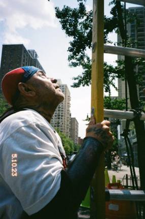 Chino Familia holds a ladder for a friend who’s hanging a Puerto Rican flag on 93rd and Columbus Ave.