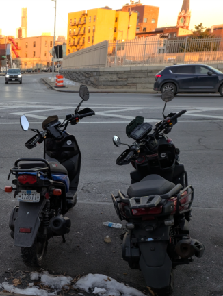 Mopeds outside a Red Hook, Brooklyn, migrant hotel, Dec. 26, 2024. One has a license plate, the other doesn’t. Similar scenes are repeated uncountably often throughout the city anywhere deliver vehicles congregate.