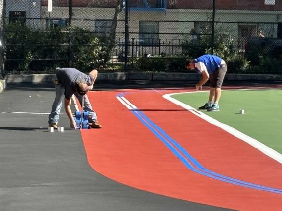 Parks Dept workers painting the lines around a new track that has appeared for the first time inside what was long known as the skateboard park that also housed a baseball diamond and basketball courts in the northern end of Tompkins Sq. Park.