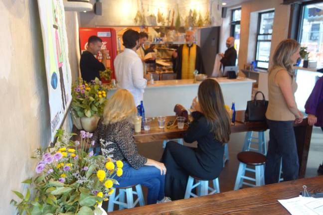 A young crowd (foreground) appears to be embracing a new Greek restaurant with old world recipes from as three Greek Orthodox priests in background finish bestowing a blessing at the grand opening celebration.