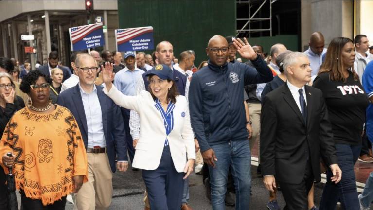 Governor Hochul flanked by Manhattan Borough Presidents Mark Levine (left)and Queens Borough president Donovan Richards (right in dark suit) with AG Letitia James at right in the “1973” sweatshirt. A lonely Mayor Adams can be seen trailing behind. The word on his blue baseball cap is “LOVE.”